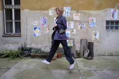 Adina Chmelová zachytená v skoku na dvore, kde býva. V pozadí sú jej diela, 2022 (foto: Rozálie Kirschová)
