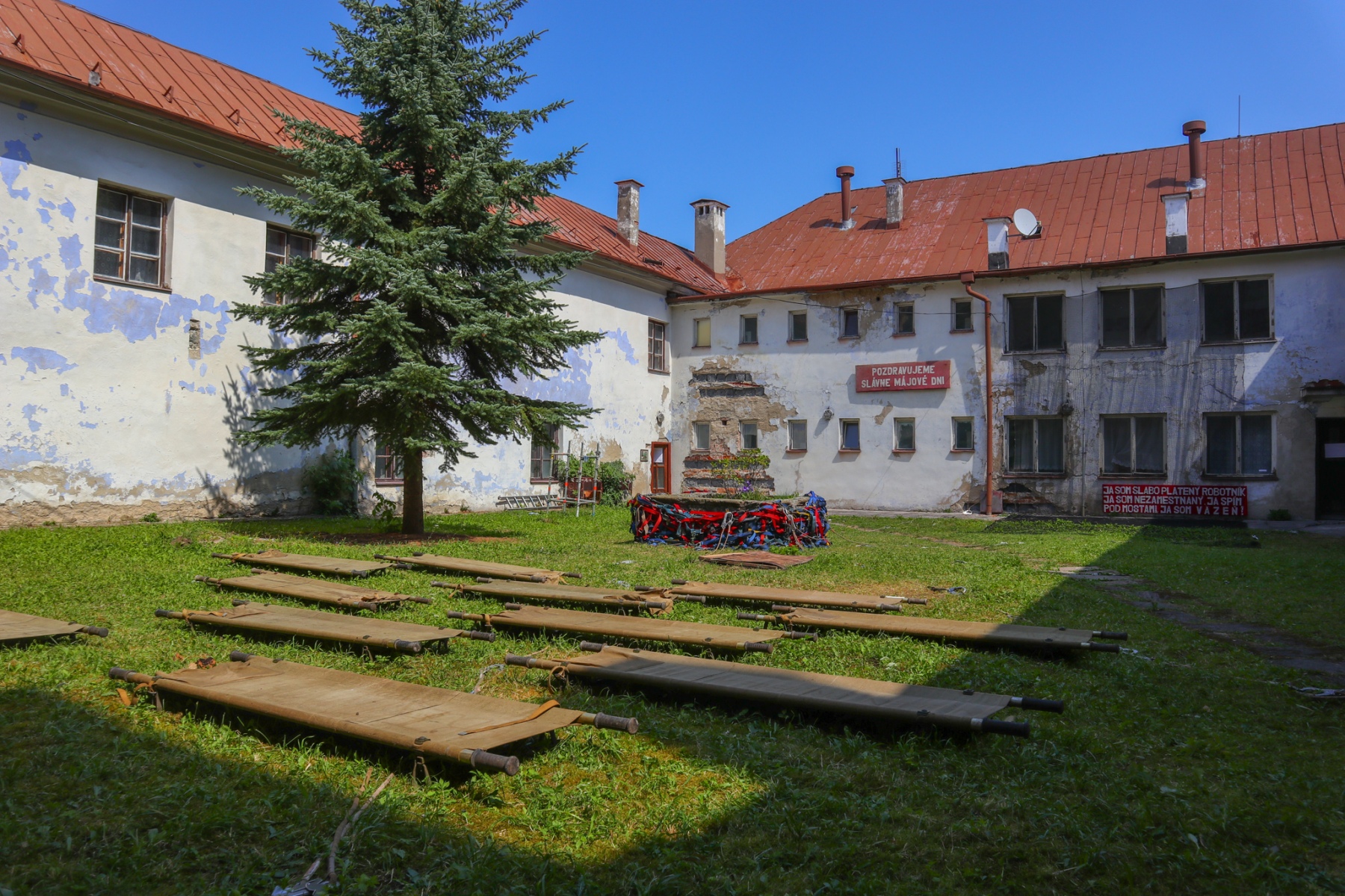 Site-specific inštalácia z ležadiel v popredí a site-specific inštalácia na fasáde budovy, 2020, Kláštor Opening, Kláštor Hieronymitánov, Štiavnické Bane. Na oboch inštaláciách sa podieľal Jakub Cmarko spolu s Magdalénou Masárovou. V Inštalácii z ležadiel chceli poukázať na nezrealizovaný projekt nemocnice pre baníkov. Na ležadlách sú nápisy z nájdených Katolíckych novín. V inštalácii na fasáde socialistickej prístavby kina reagovali jej prikrytím sieťou na nezmyselné pripojenie k budove fary. Na fasáde sa nachádzajú aj dva transparenty – jeden je pôvodný socialistický slogan nájdený na povale budovy, druhý vyrobili umelci spoločne z útržkov textov z Katolíckych novín, v ktorom reagujú na nezmyselnosť pôvodného nápisu. (foto: KUNSTARTUM)