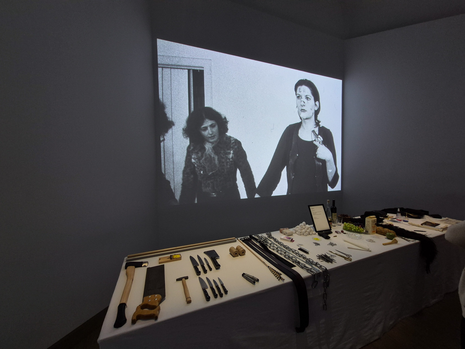 Marina Abramović: Rhythm 0, 1974, 6 hodinová performance – stôl, obrus a 72 objektov, Studio Morra, Neapol; projekcia bez zvuku + stôl s predmetmi použitými počas performance Rhythm 0. (foto: KUNSTARTUM)